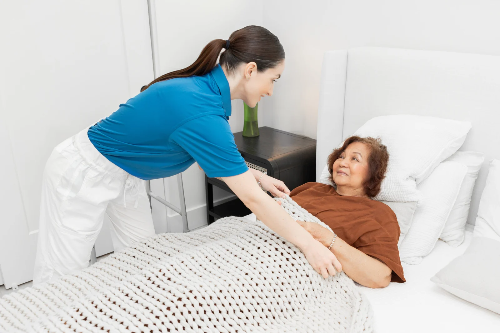 An Aloha caregiver gently helping a senior woman settle comfortably in bed at home