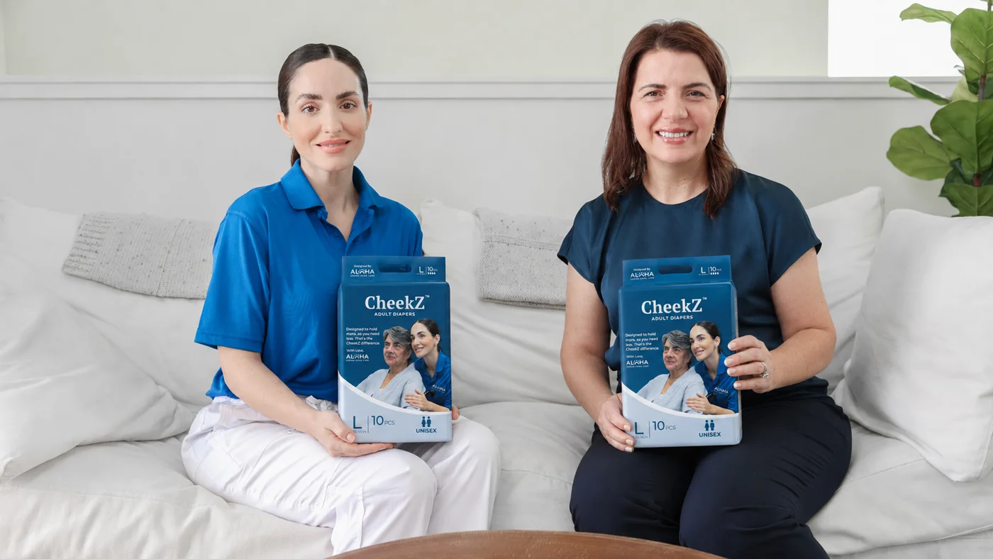 Two members of the Aloha team holding CheekZ adult diaper packs at a senior's home in San Diego