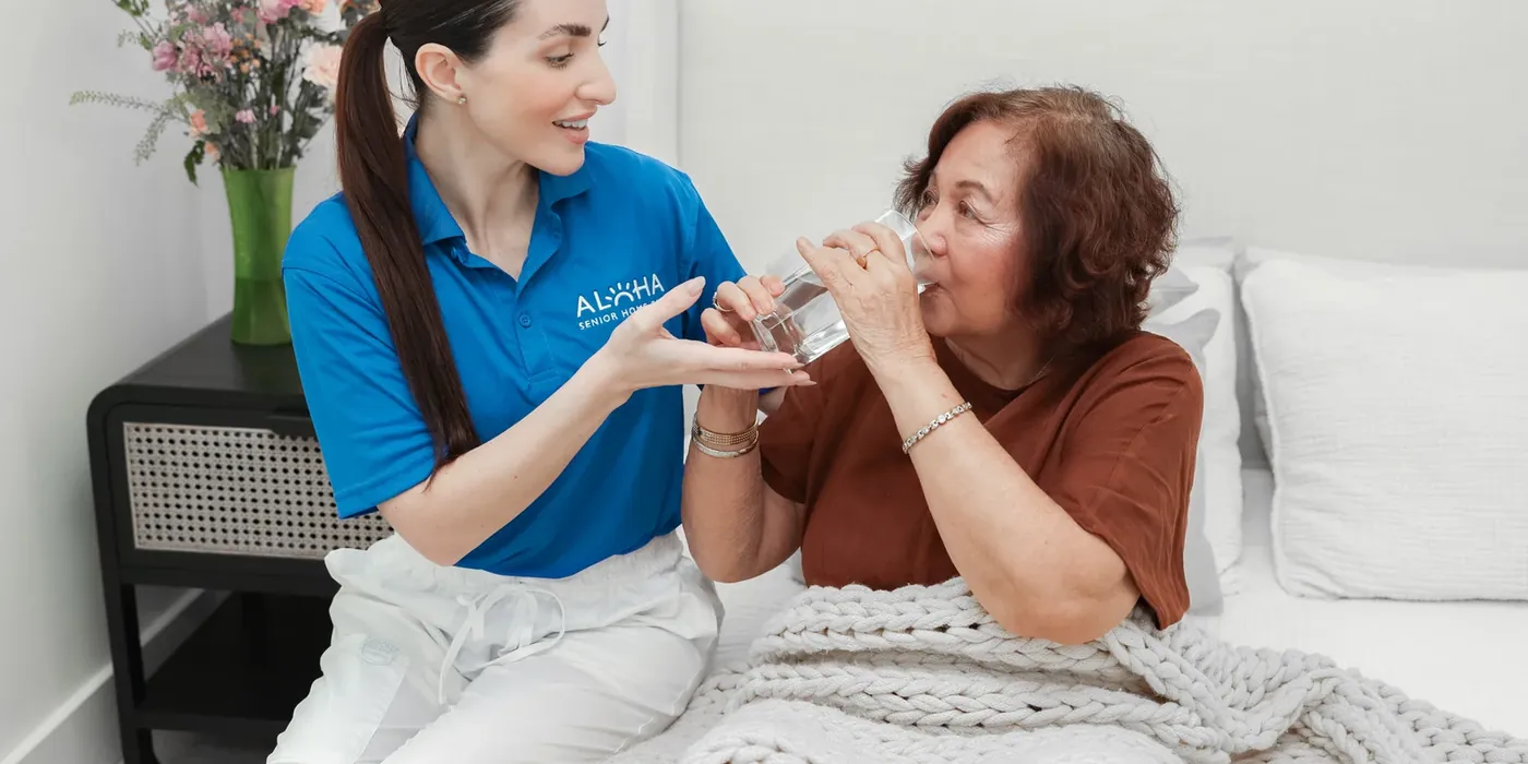 An Aloha caregiver helping a senior woman with a glass of water at home in San Diego